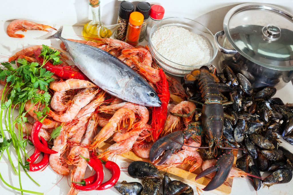 sur une table de cuisine sont disposés des crevettes, un maquereau, un homard et des moules